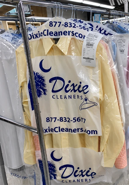 Yellow dress shirt covered in a clear Dixie Cleaners bag hangs on a rack with other cleaned garments. Cleaning receipt is attached to the hanger.