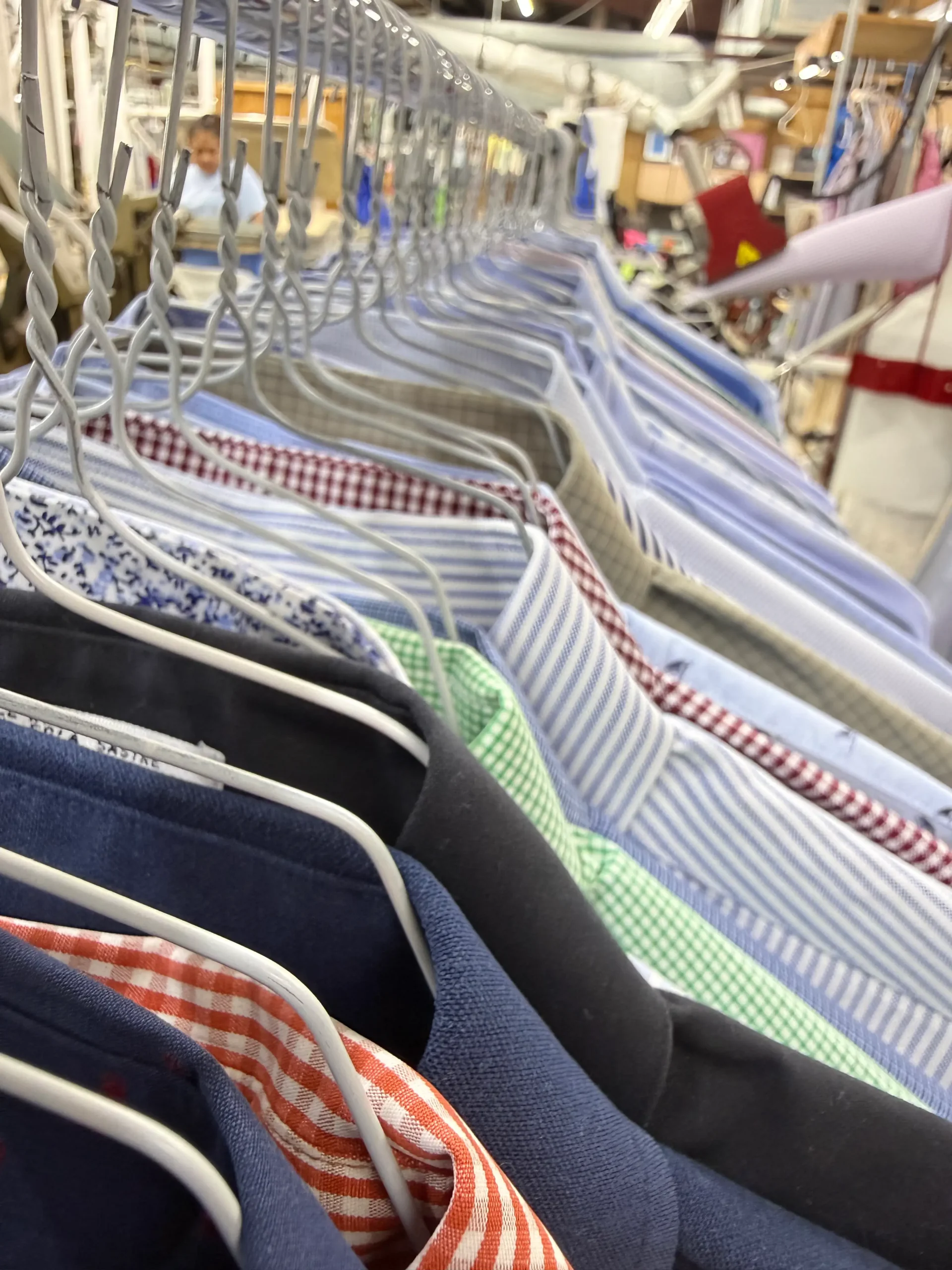 A row of assorted men’s dress shirts on hangers in a clothing store or laundry facility, shown from a close, angled perspective.